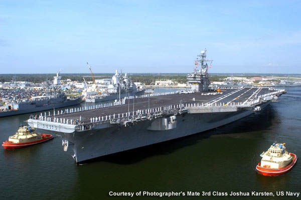 An aircraft carrier is escorted by tugs at Naval Station Mayport.